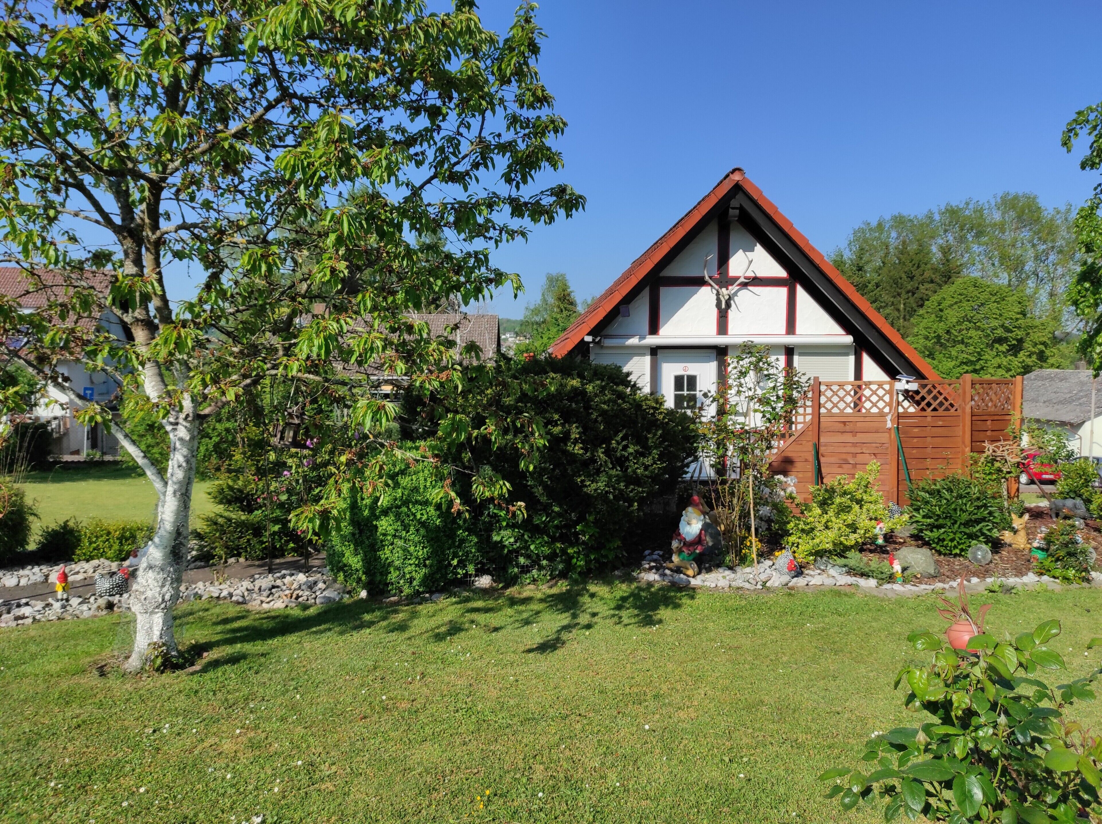 Ein zweistöckiges Haus mit geneigtem Dach, umgeben von einem gepflegten Garten mit verschiedenen Pflanzen und einer Rasenfläche.