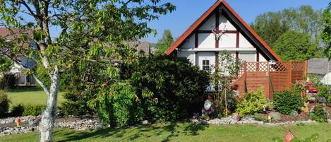 Ein zweistöckiges Haus mit geneigtem Dach, umgeben von einem gepflegten Garten mit verschiedenen Pflanzen und einer Rasenfläche.