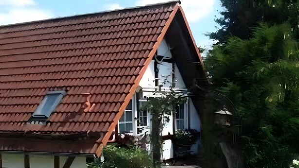 Uma casa com telhado de telhas vermelhas, um caminho que leva à entrada e um jardim com decorações esféricas brancas.