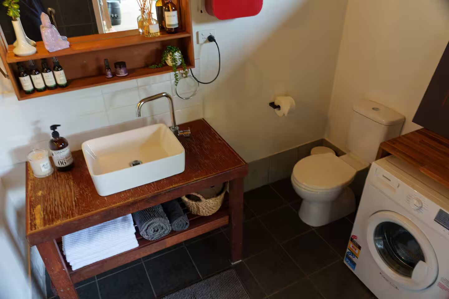 Une petite salle de bain avec un meuble-lavabo en bois, un lavabo blanc, des toilettes et un lave-linge.
