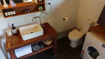 Une petite salle de bain avec un meuble-lavabo en bois, un lavabo blanc, des toilettes et un lave-linge.