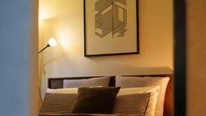 Una cama bien tendida con ropa de cama a rayas, una obra de arte mural geométrica y una lámpara de noche.