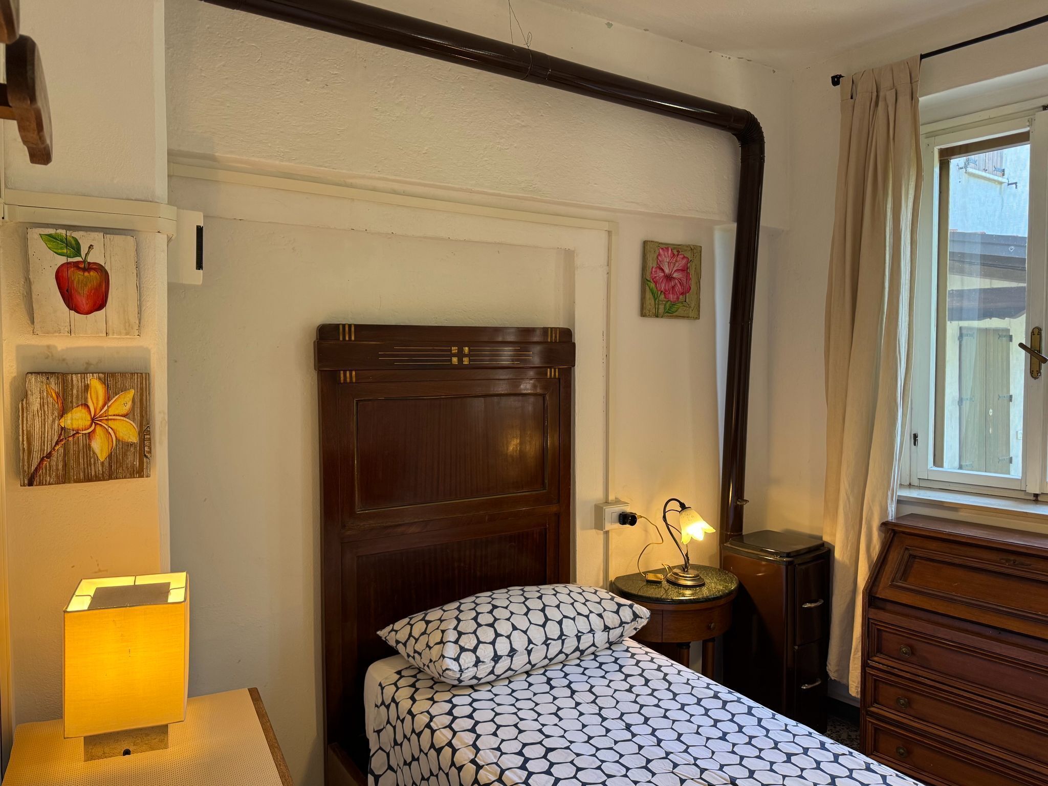 Une chambre à coucher avec une tête de lit en bois, un lit recouvert d’une literie à motifs, une lampe de chevet, une table de chevet et des œuvres d’art accrochées aux murs.