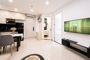 A modern living room with a flat-screen TV, a dining area with a table and chairs, and a kitchen area with cabinets and appliances. - Sun Residences Hotel and Apartment (Hanoi)