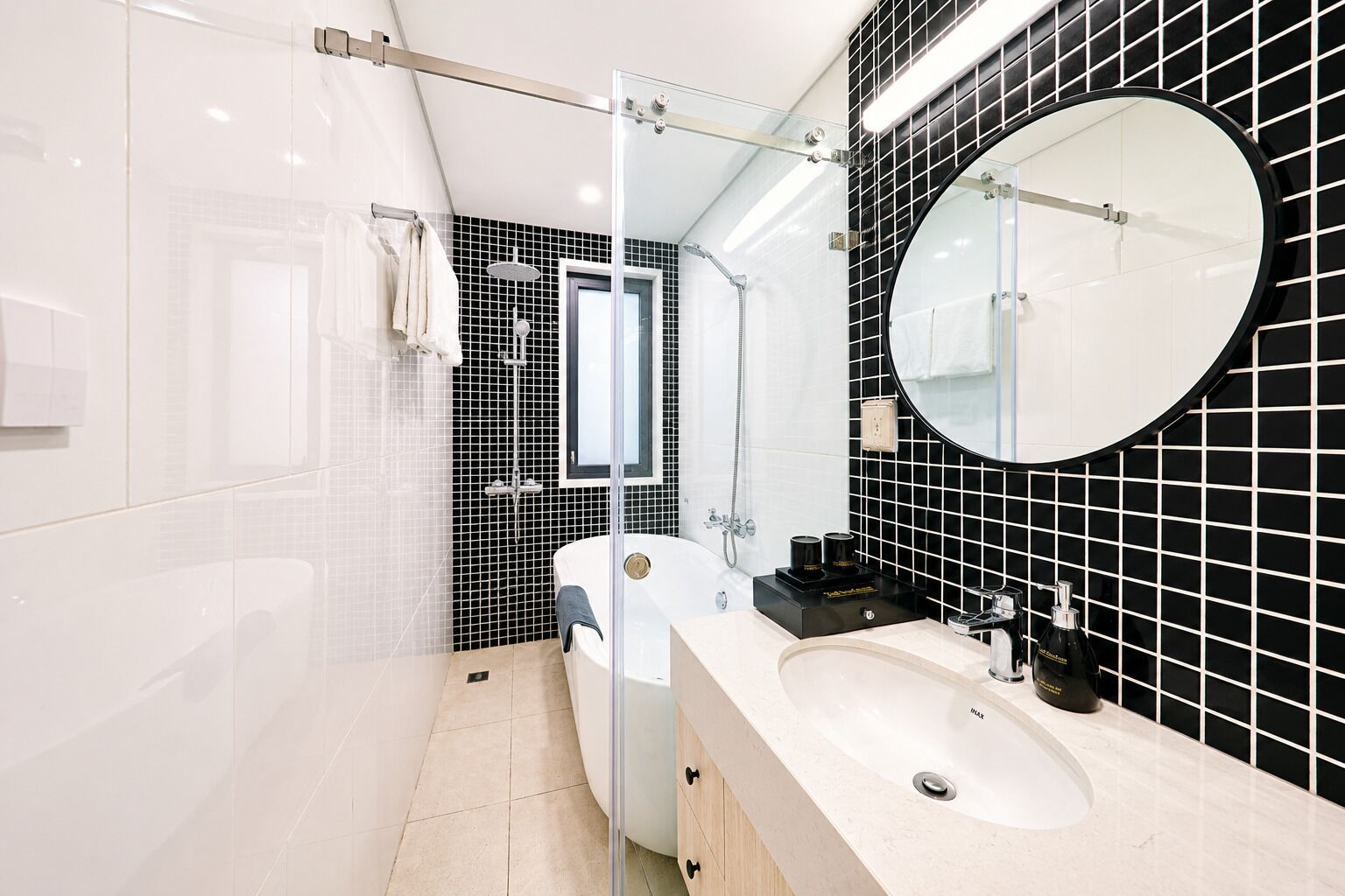 A modern bathroom with a glass shower enclosure, a bathtub, a large round mirror, and a vanity with a sink.