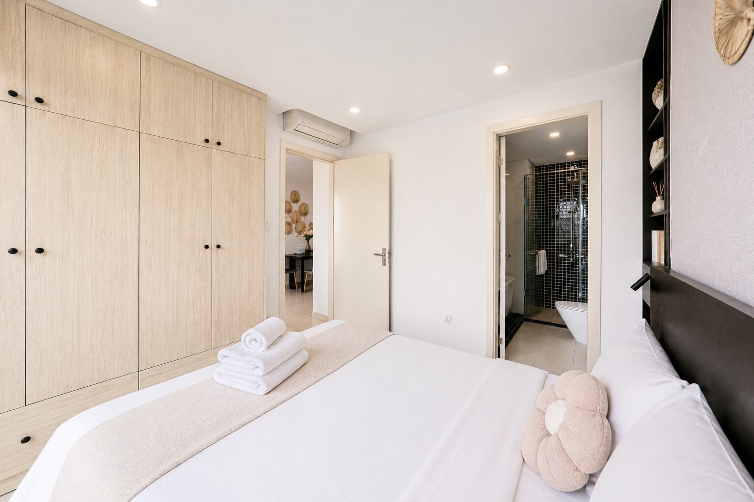Un dormitorio moderno con una cama grande, un armario de madera y un baño visible a través de una puerta abierta.