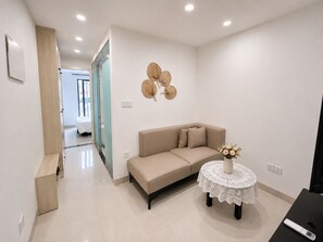 Un salon moderne avec un canapé beige, une petite table ronde recouverte d’une nappe blanche en dentelle et un élément décoratif mural.