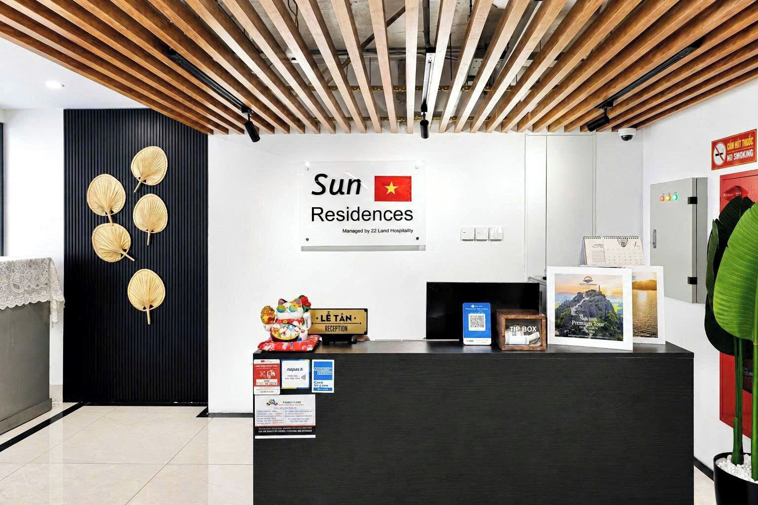 Uma mesa de recepção com a placa da Sun Residences, uma área de recepção e uma parede decorativa com padrões de folhas.