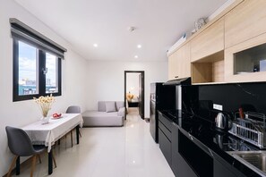 A modern kitchen with black appliances, a dining area with a table and chairs, and a sofa in the background.