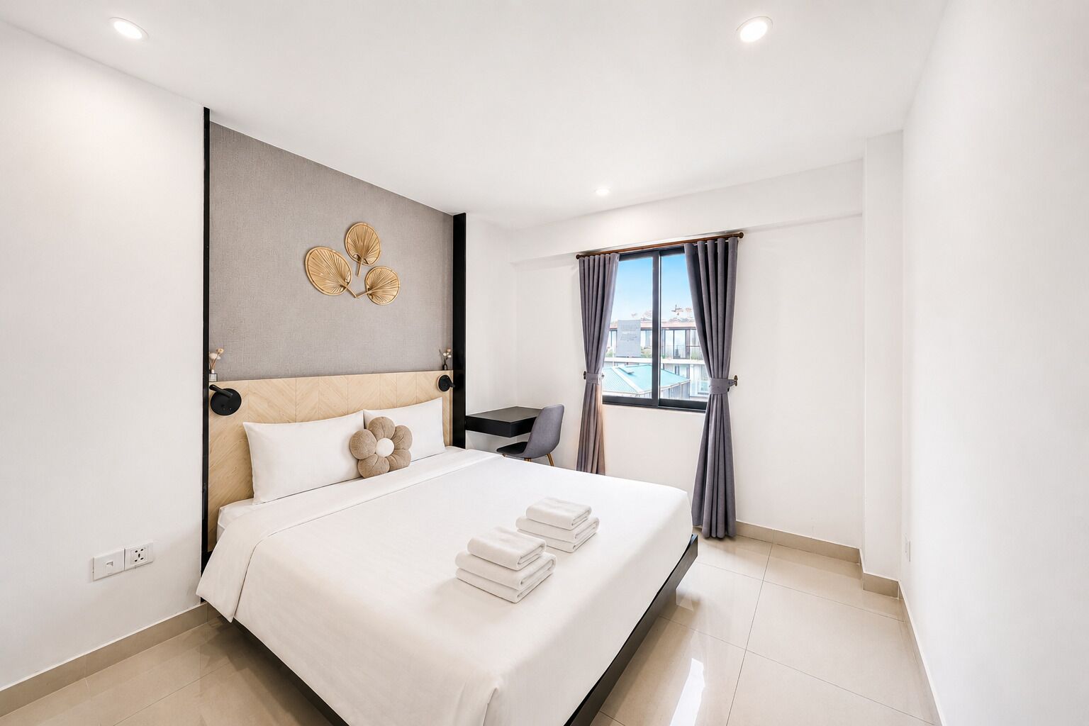 A modern hotel room with a large bed, a desk, and a view of the city through the window.