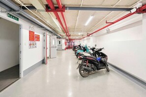 A clean, well-lit corridor with a row of parked scooters, exit signs, and fire safety posters on the walls.