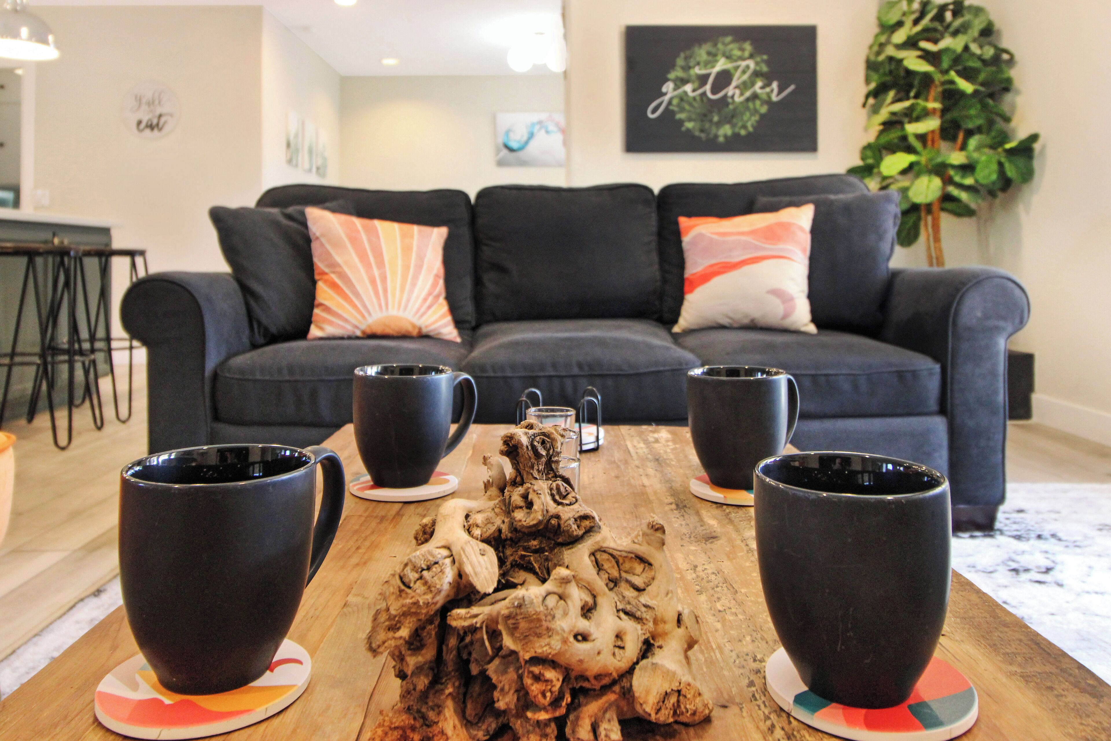 A living room with a dark blue sofa, two black coffee mugs on coasters, and a wooden table with a decorative centerpiece.