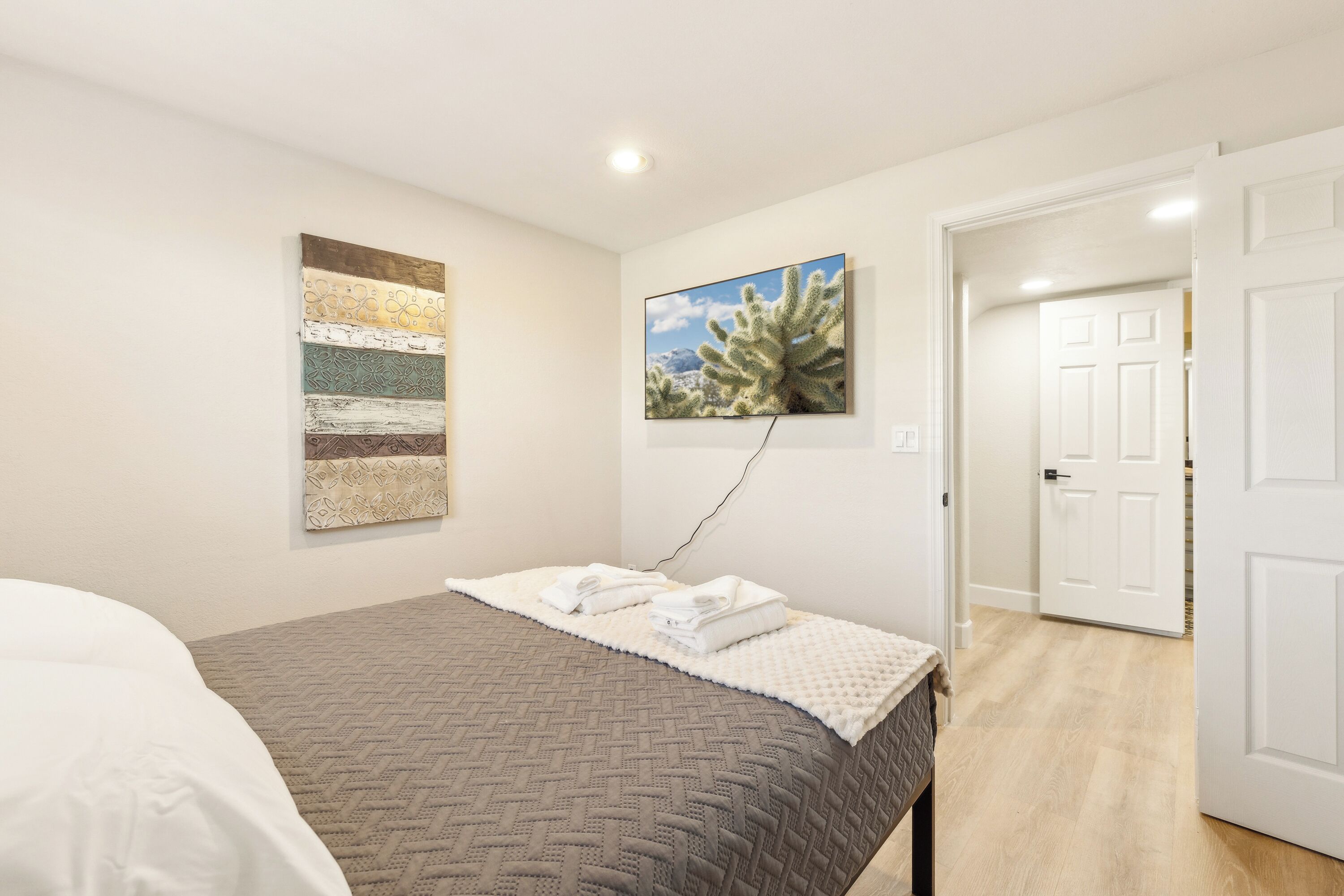 A bedroom with a bed, a wall-mounted artwork, and a door leading to another room.