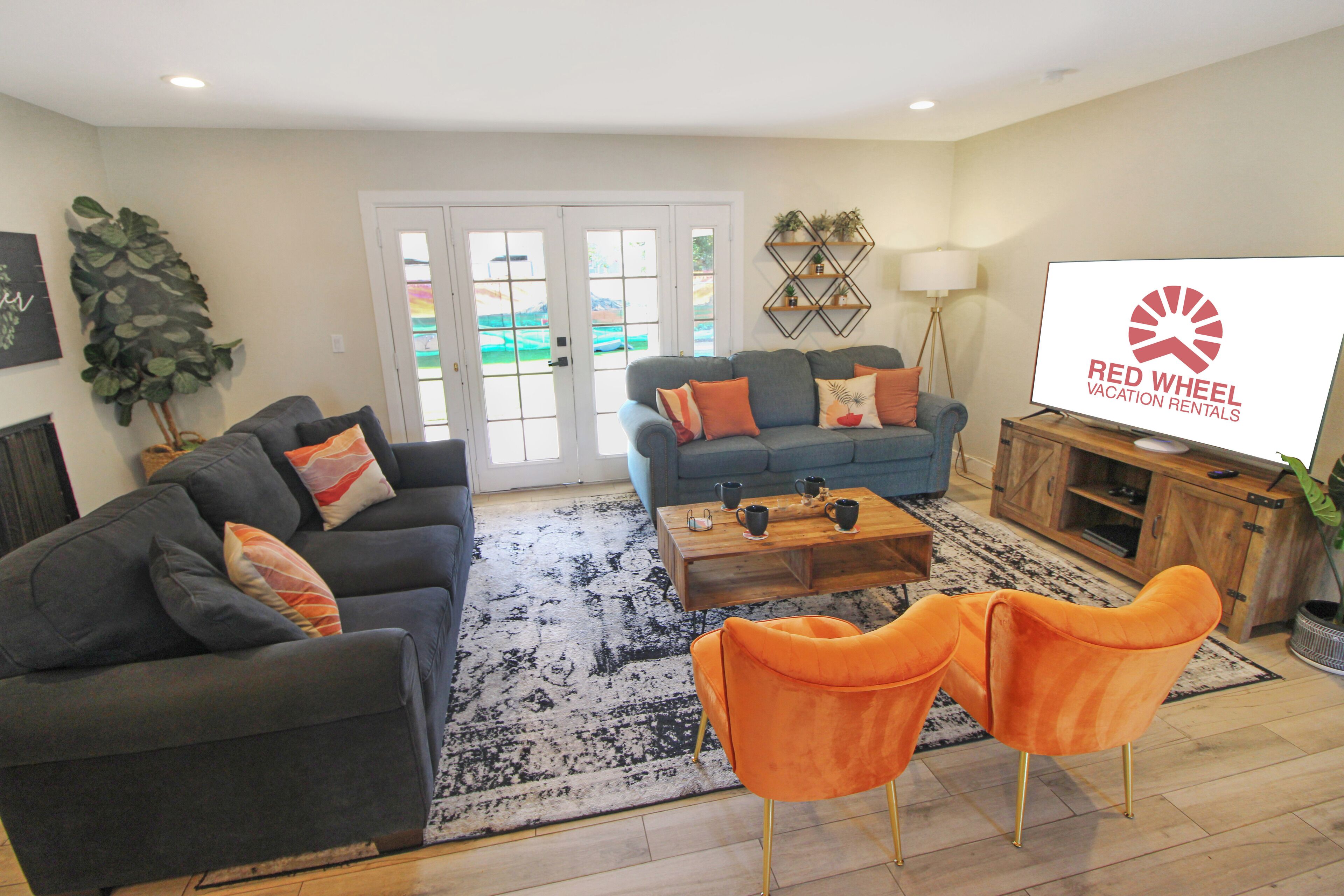 A living room with two sofas, a coffee table, and a TV. There is a large window with a view of a garden.
