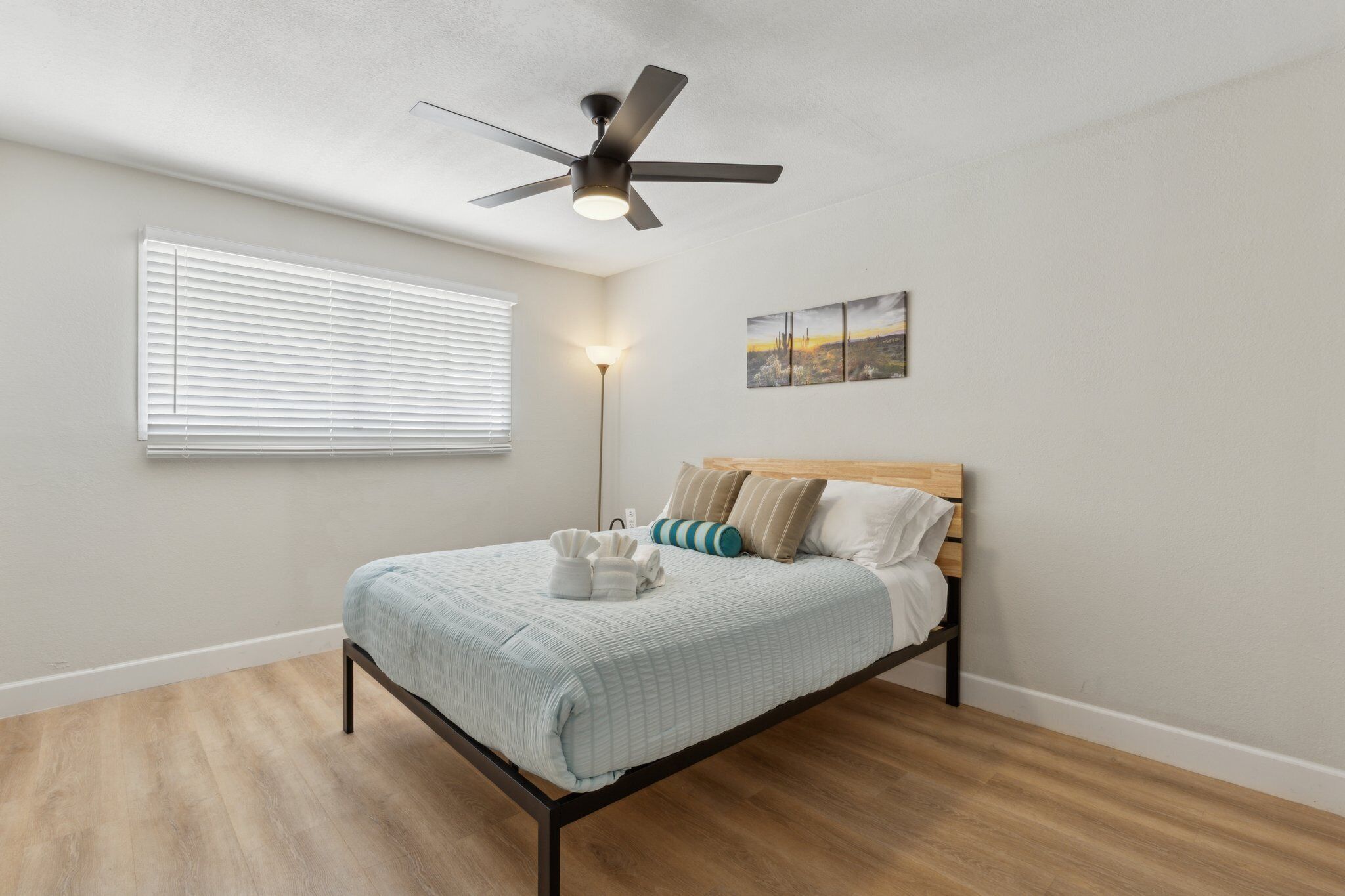A bedroom with a bed, a ceiling fan, a bedside lamp, and a window with blinds.