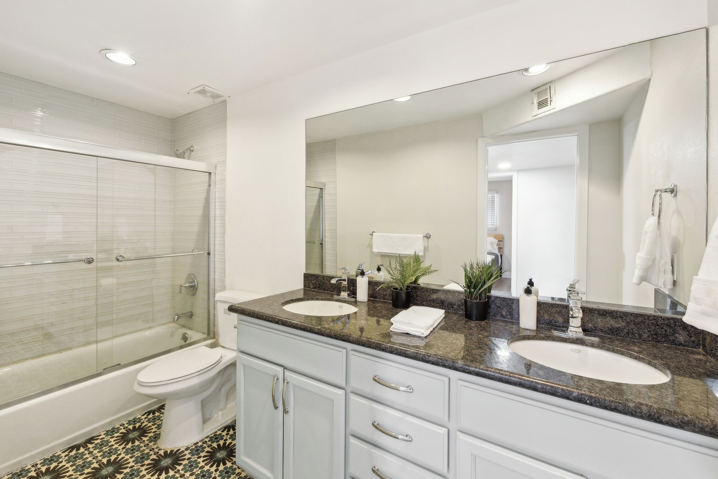 Un baño moderno con ducha de vidrio, dos lavamanos y un espejo grande.