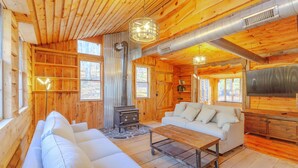 Acogedor interior de cabaña de troncos con sofá, una mesa de centro, chimenea y televisor.