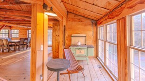 Interior de una cabaña de madera con comedor, banco y estufa.