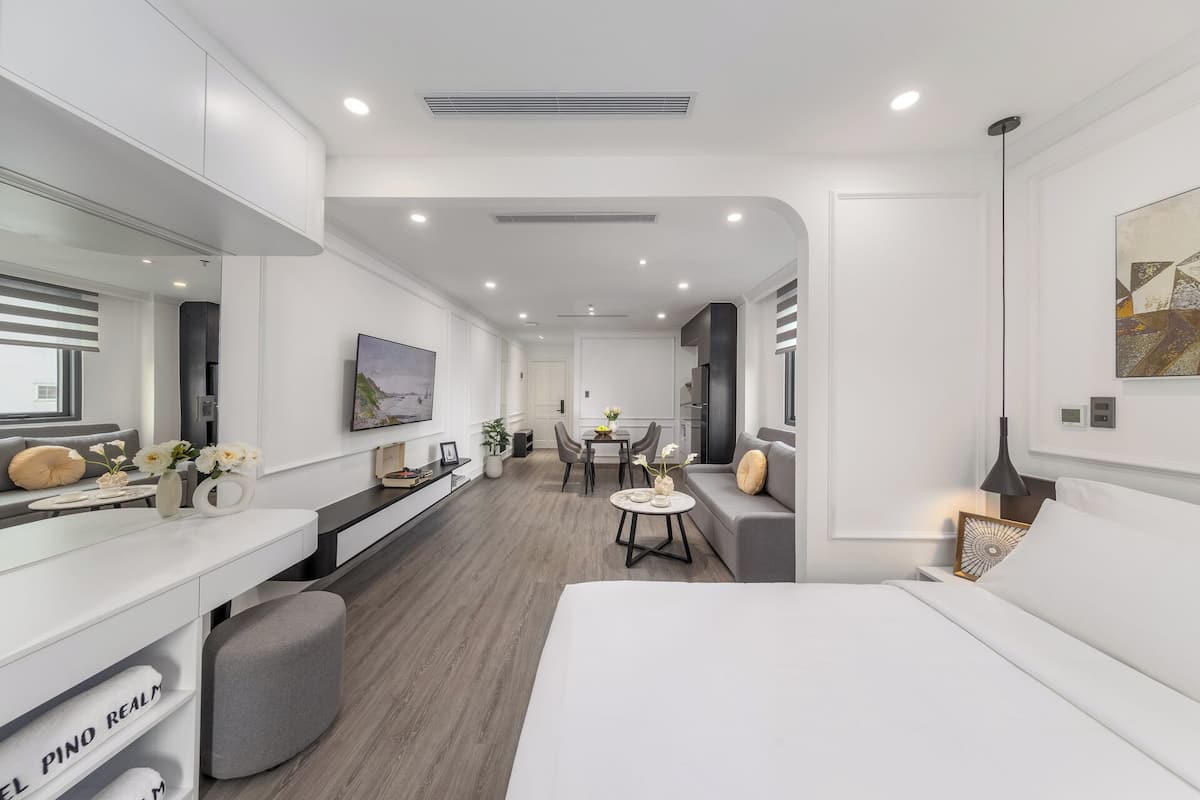 Une chambre d’hôtel moderne dotée d’un grand lit, d’un bureau avec un ordinateur, d’un coin salon avec une table et des chaises, et d’une grande fenêtre.