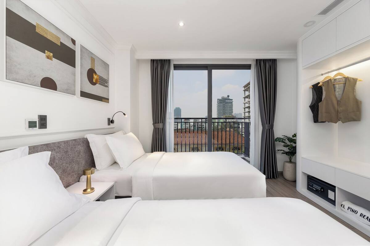 Une chambre d’hôtel moderne dotée d’un grand lit, d’une table de chevet avec une lampe, d’une armoire et offrant une vue sur la ville depuis un balcon.