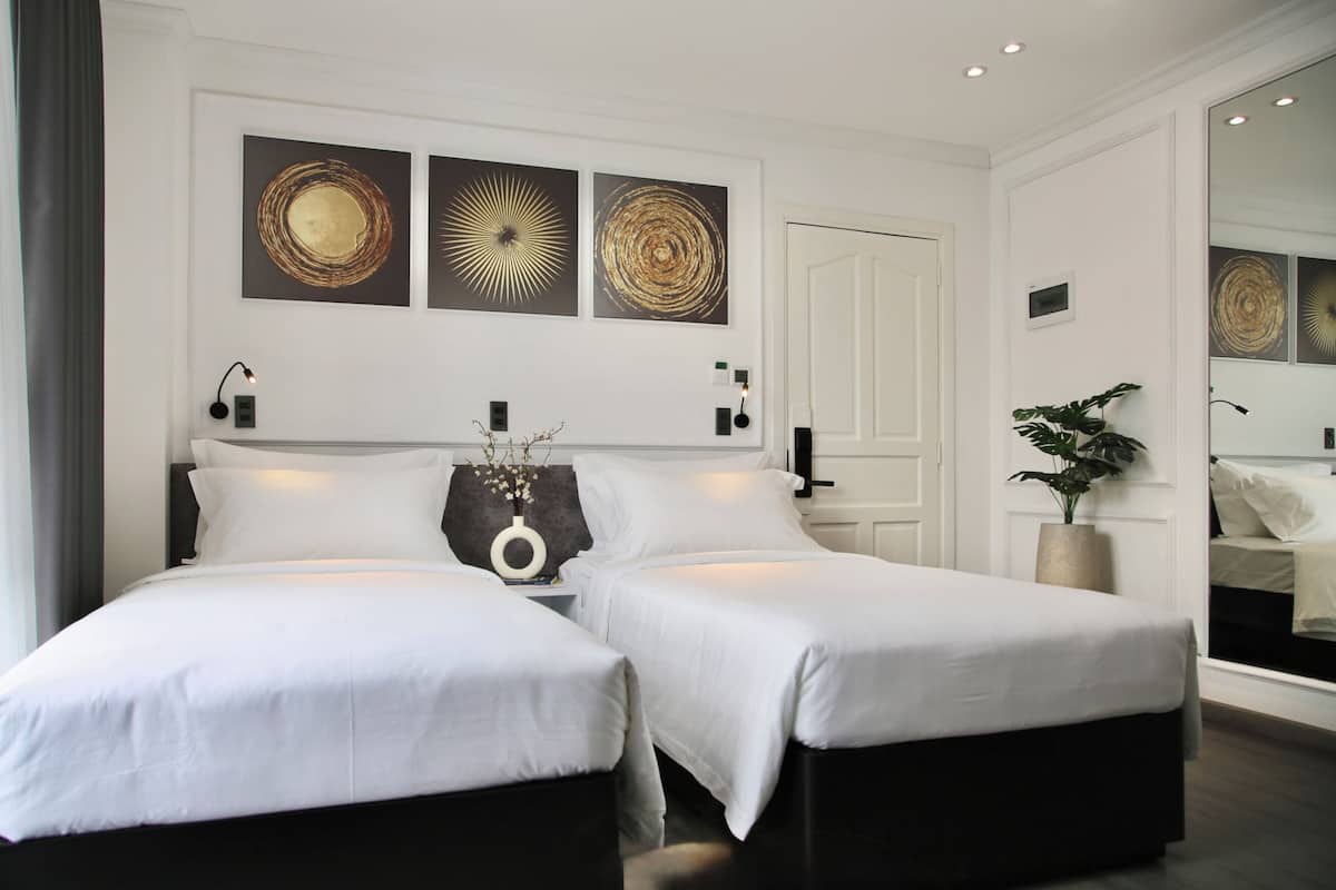 Une chambre d’hôtel avec deux lits, un grand miroir et trois œuvres d’art murales.