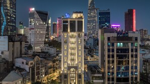 A cityscape at night with illuminated buildings, including a prominent skyscraper with a unique design and a building with a large sign. - CityHouse - El Pino Realm at Metro Ben Thanh Market (Ho Chi Minh City)