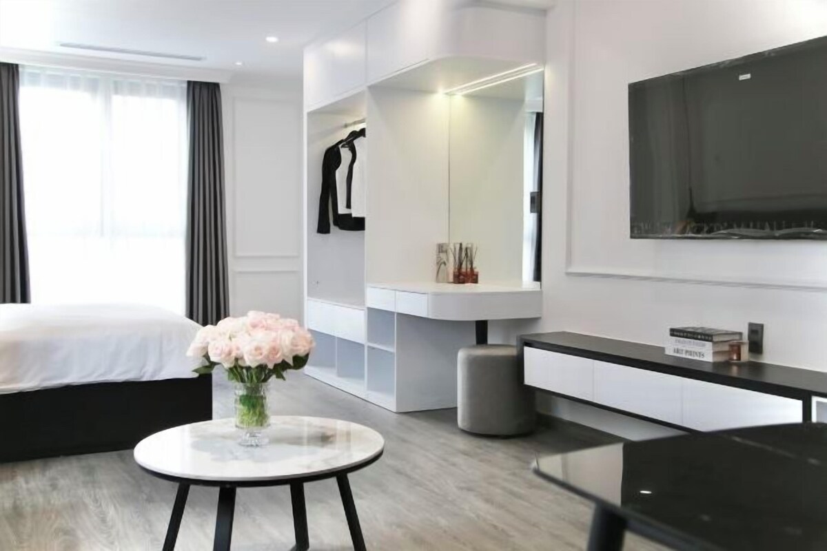 Una habitación de hotel moderna con una cama, una mesa redonda con un florero, un televisor, un armario y un escritorio con una silla.