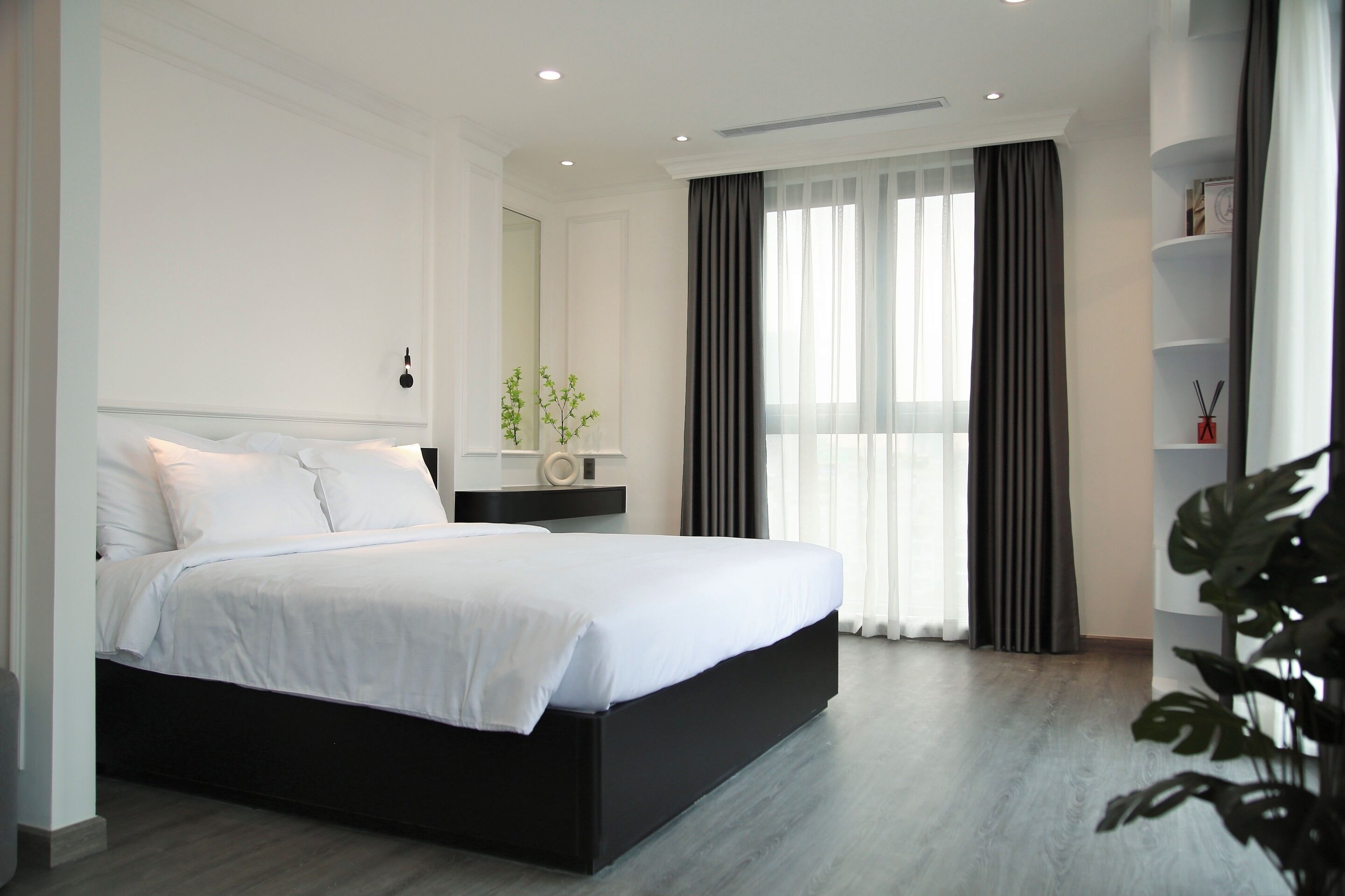 A modern bedroom with a large bed, a bedside table, a mirror, and a window with curtains.