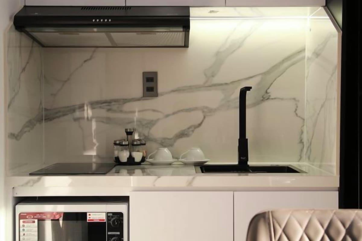 Cocina con salpicadero de mármol, extractor de aire negro, microondas y un lavamanos con grifo negro.