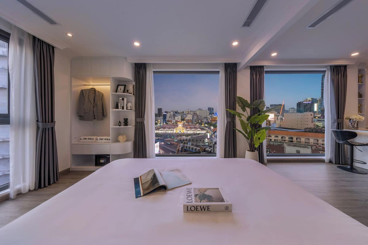 Une chambre d’hôtel moderne dotée d’un grand lit, offrant une vue sur la ville, et comprenant une bibliothèque ainsi qu’un bureau avec une chaise.