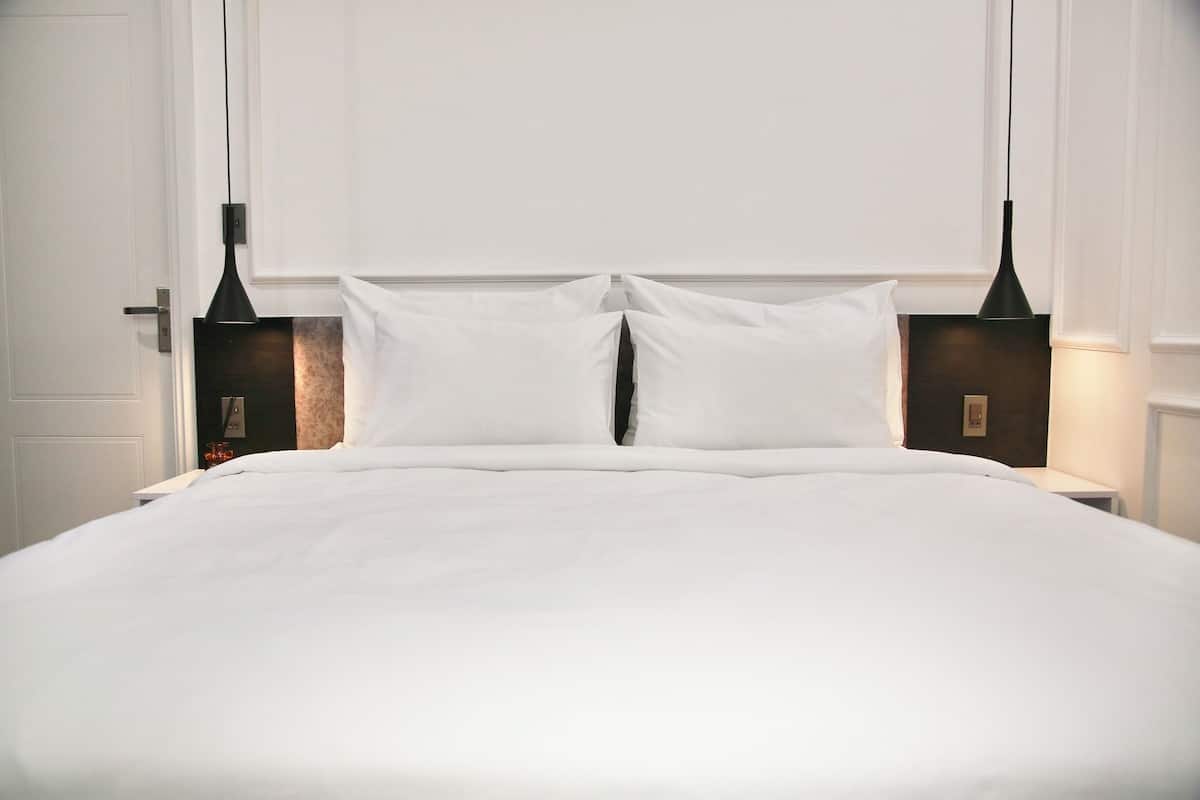 Un lit bien fait, avec du linge de lit blanc, flanqué de deux tables de chevet sur lesquelles sont posées des lampes noires.