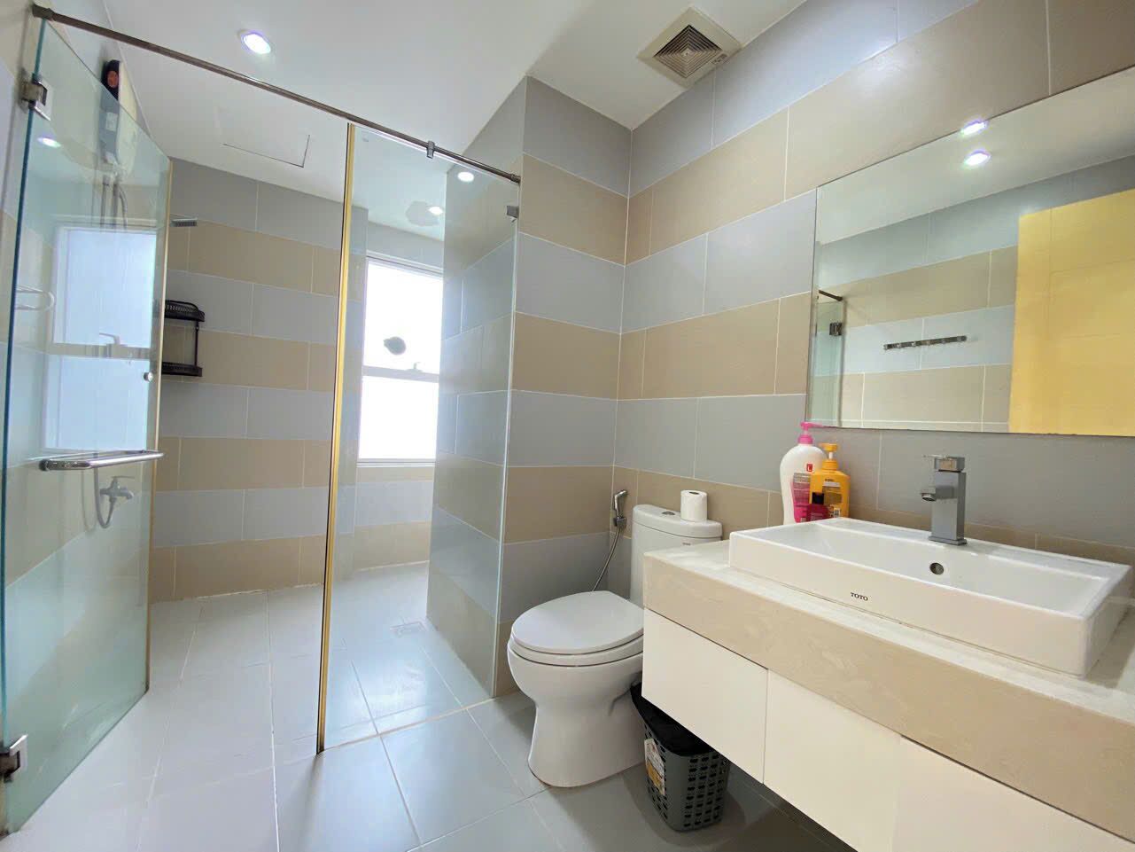A modern bathroom with a glass shower enclosure, a toilet, and a vanity with a sink and mirror.