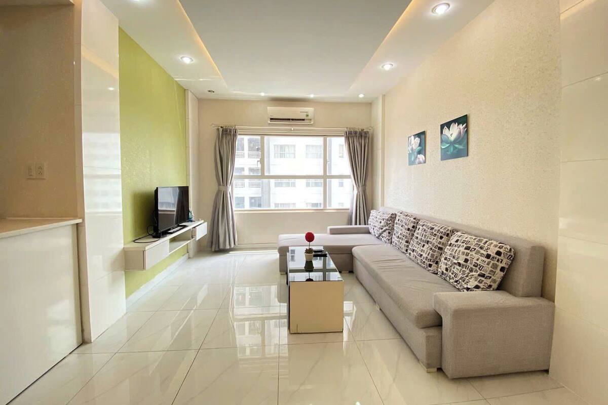 A modern living room with a sofa, a coffee table, a TV on a stand, and a window with curtains.