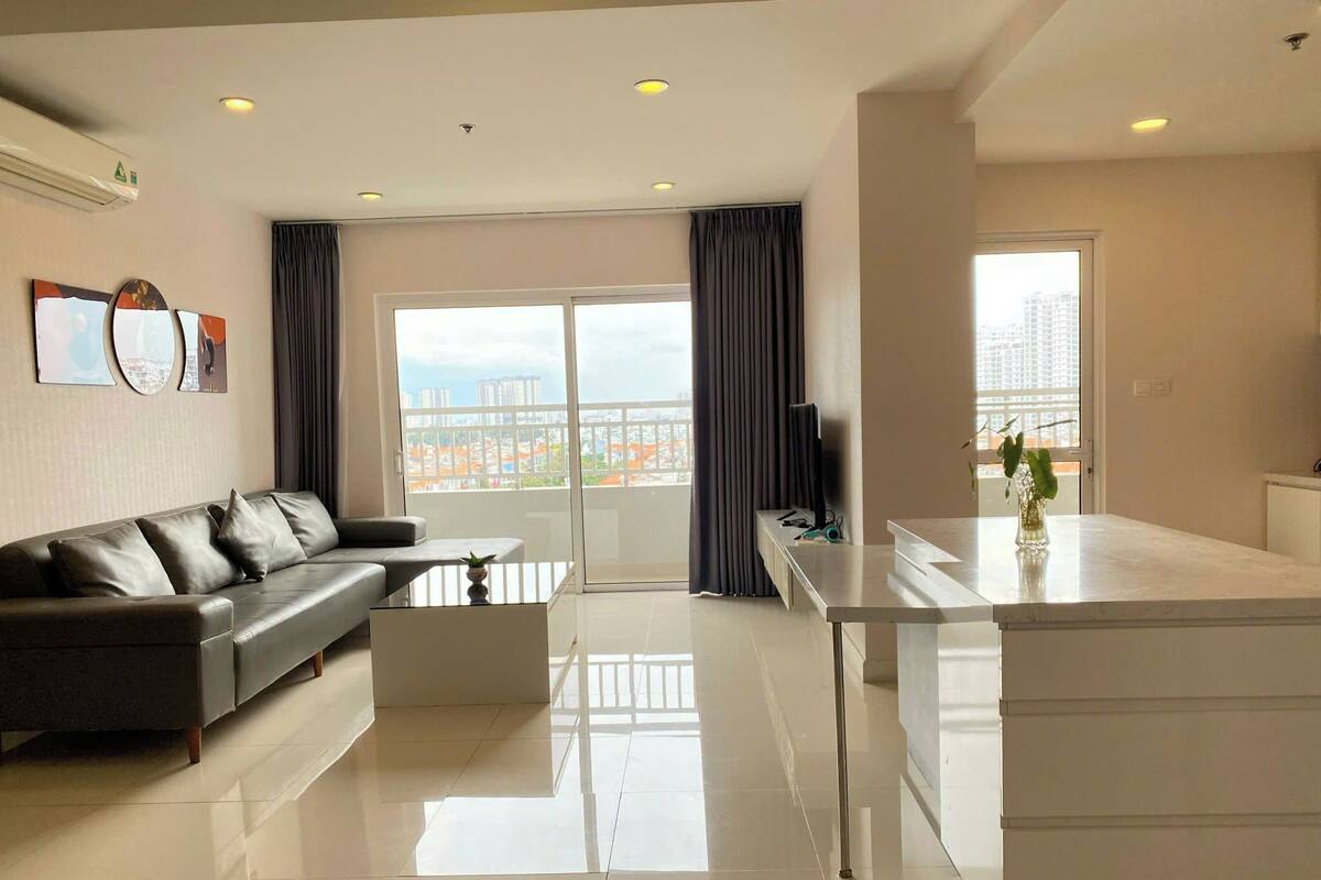 A modern living room with a sofa, a coffee table, and a kitchen area with a counter and a plant.