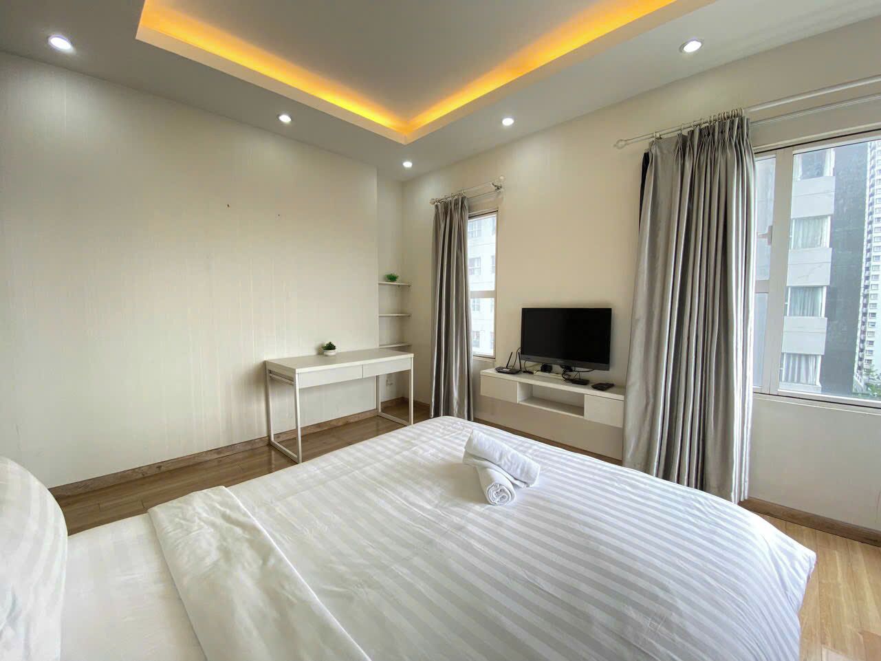 A hotel room with a bed, a desk, a TV, and a window with curtains.