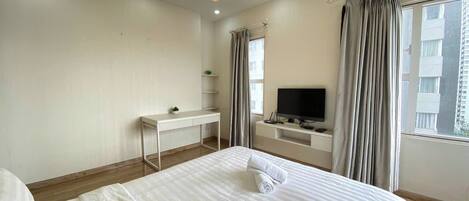 A hotel room with a bed, a desk, a TV, and a window with curtains.