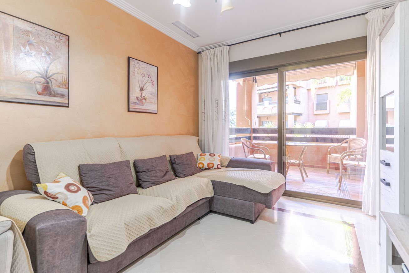 A modern living room with a sectional sofa, a large window with a view of a balcony, and two framed artworks on the wall.