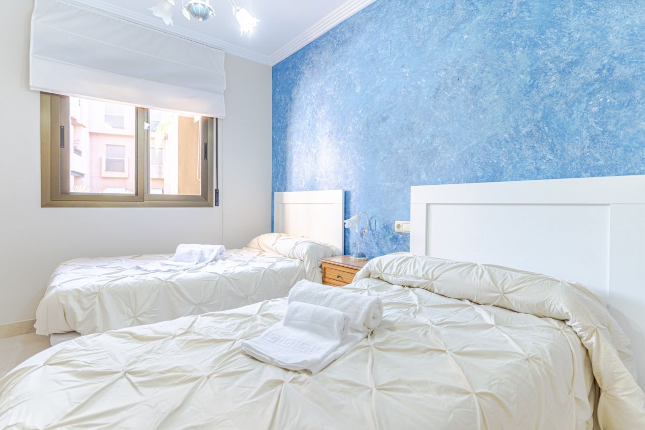 A bedroom with two beds, a window, and a blue textured wall.