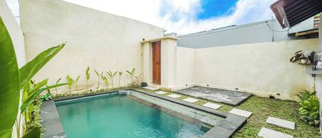 A swimming pool with a tiled deck, surrounded by a low wall and potted plants.
