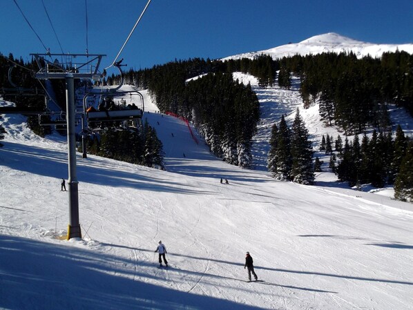 Une piste de ski avec un télésiège, des arbres et une montagne enneigée en arrière-plan.