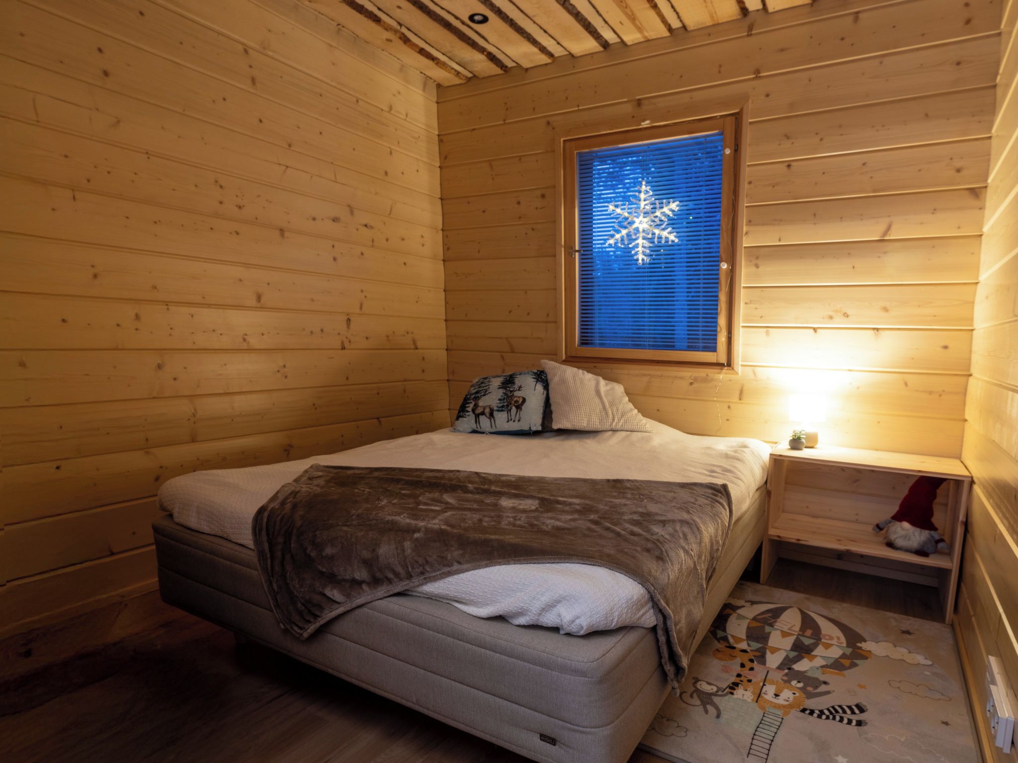 A cozy wooden cabin room with a bed, a nightstand, and a window with blinds.