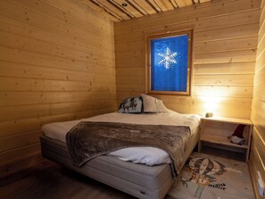 Habitació acollidora d'una cabana de fusta amb un llit, una taula de nit i una finestra amb persianes.