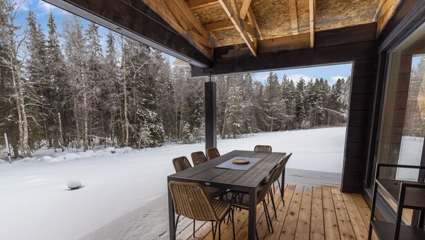 Una terraza de madera con una mesa y sillas, con vistas a un paisaje nevado con árboles.