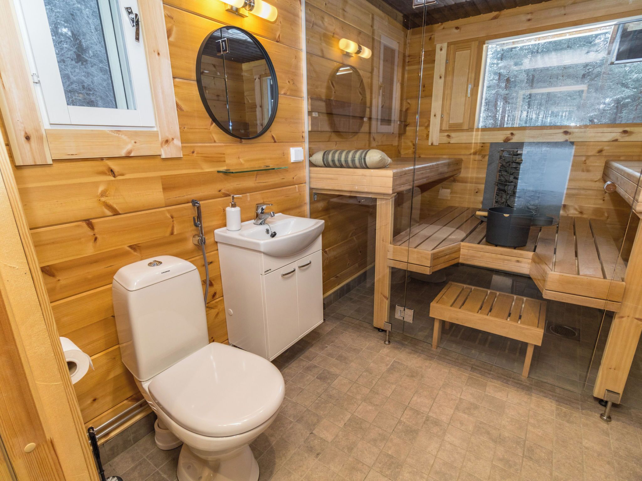 A wooden cabin bathroom with a toilet, sink, and shower area.