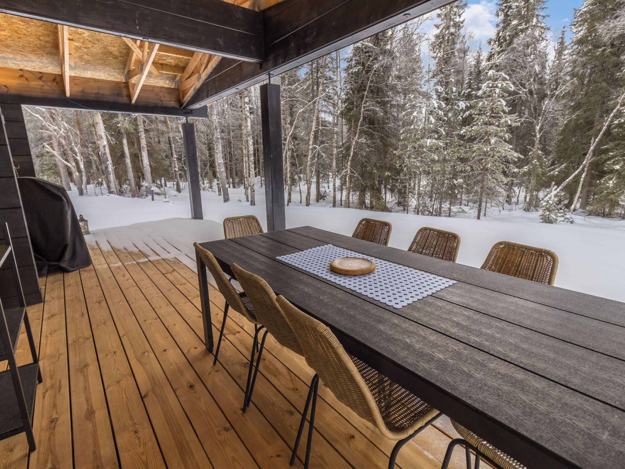 A wooden deck with a table and chairs, overlooking a snowy forest.