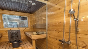 Una cabaña de madera con mampara de vidrio para la ducha, un banco de madera y una mesa con hervidor y olla.