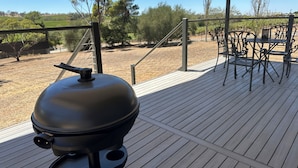 A barbecue grill on a wooden deck with a view of a vineyard and trees.