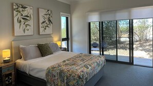 A bedroom with a bed, a nightstand, a ceiling fan, and a large window with a view of trees and a body of water.