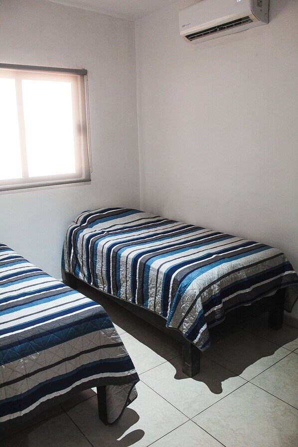 A room with two single beds, a window, and an air conditioning unit.