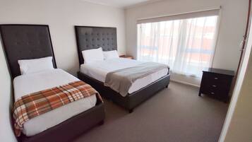 A hotel room with two beds, a large window with sheer curtains, and a small dark dresser.
